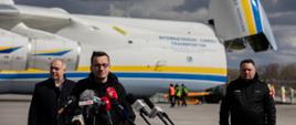 Premier Mateusz Morawiecki, Jacek Sasin i Marcin Chludziński podczas briefingu na tle samolotu.