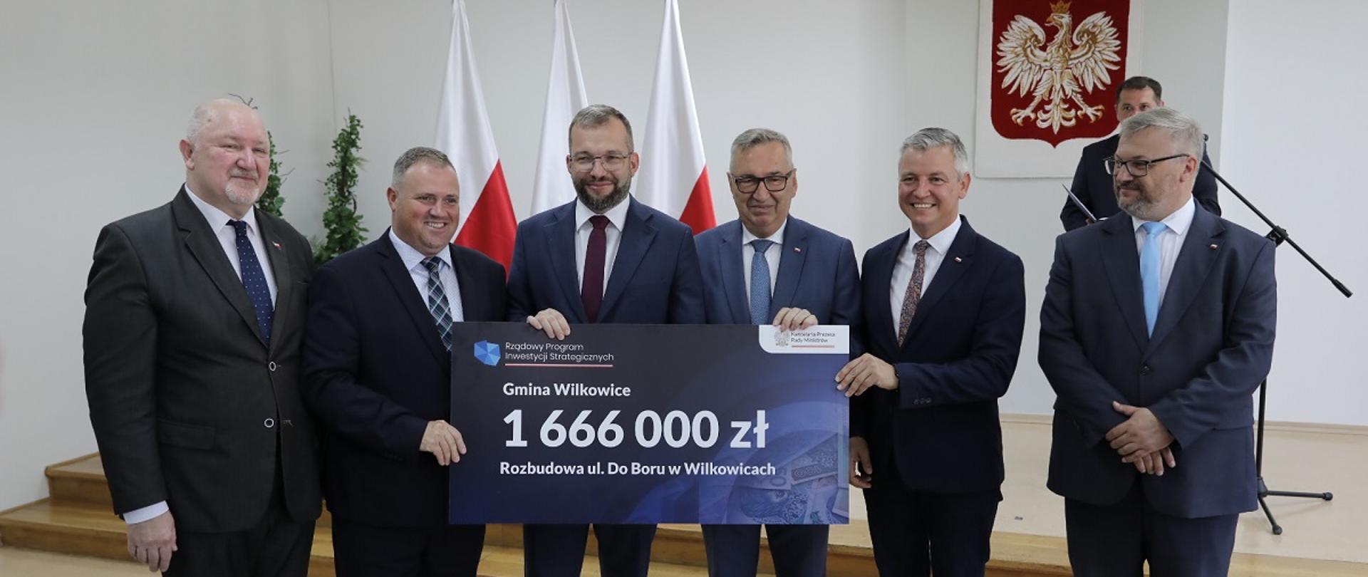 Minister funduszy i polityki regionalnej Grzegorz Puda podczas wręczenia promes dla podbeskidzkich gmin, które otrzymały dofinansowanie z Rządowego Programu Inwestycji Strategicznych, minister stoi i trzyma w dłoniach promesę dla gminy Wikowice, po jego prawej stronie wiceminister rodziny i polityki społecznej Stanisław Szwed