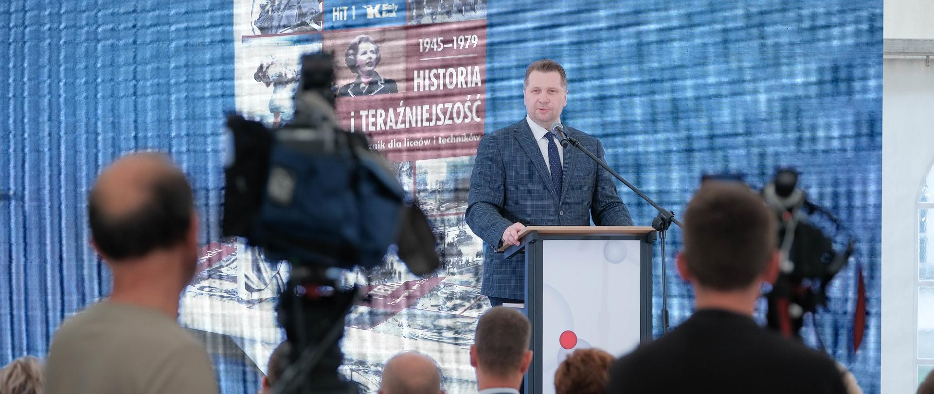 Minister Czarnek stoi na mównicy i mówi do mikrofonu.