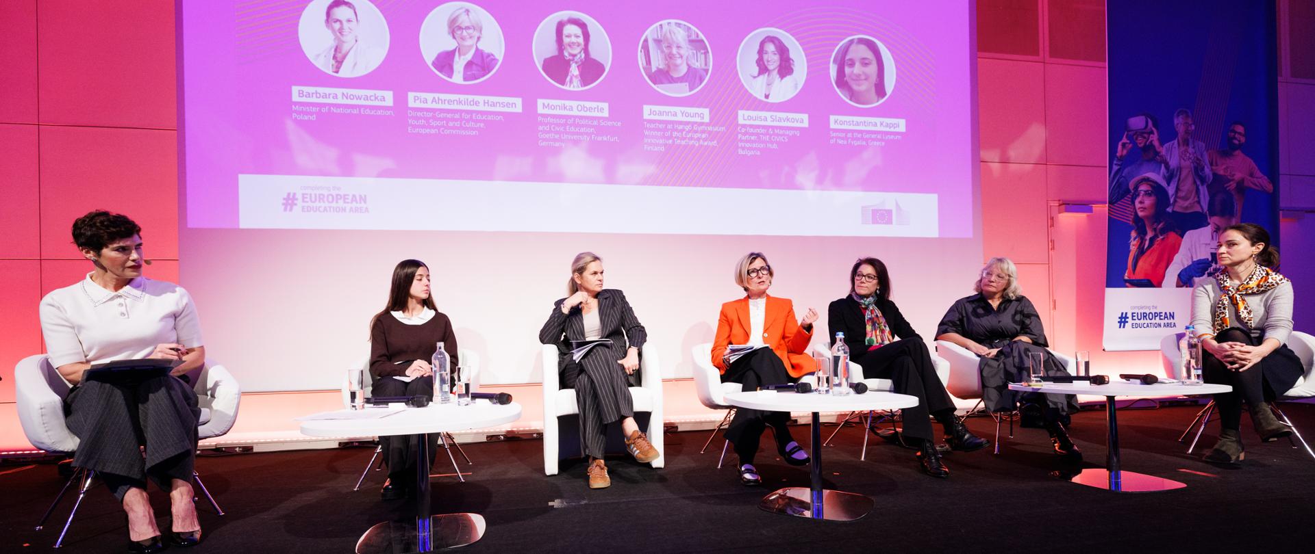 Zdjęcie panelu dyskusyjnego na scenie w trakcie European Education and Skills Summit 2025. Siedem kobiet siedzi na białych fotelach. W tle widoczny jest duży ekran, na którym wyświetlony jest tytuł sesji "How can citizenship education strengthen Europe’s democracy and resilience?" oraz zdjęcia i nazwiska panelistek, w tym Barbary Nowackiej i Pii Ahrenkilde Hansen.
