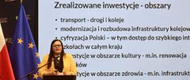 Minister funduszy i polityki regionalnej Małgorzata Jarosińska-Jedynak stoi przy pulpicie i przemawia do mikrofonu, za jej plecami grafika z prezentacją