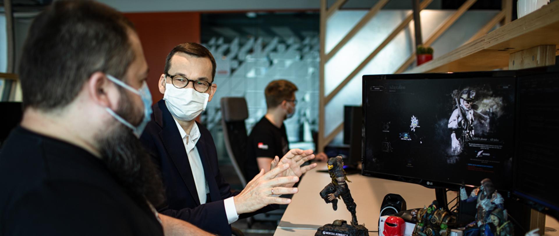 Premier siedzi przy biurku z pracownikiem.