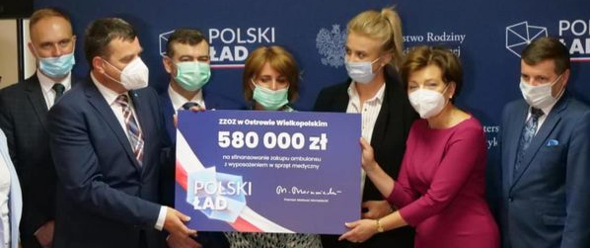 Zdjęcie grupowe. Osoby trzymają w dłoniach czek, symbolicznie przekazujący wsparcie finansowe. Napis 580 000 zł.