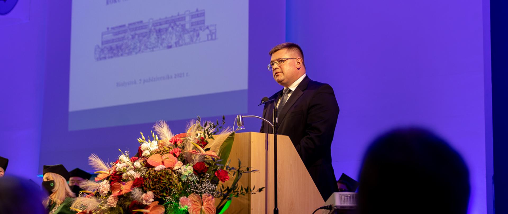 Sekretarz Stanu w MEiN Tomasz Rzymkowski stoi przy pulpicie. Przed nim wieniec.