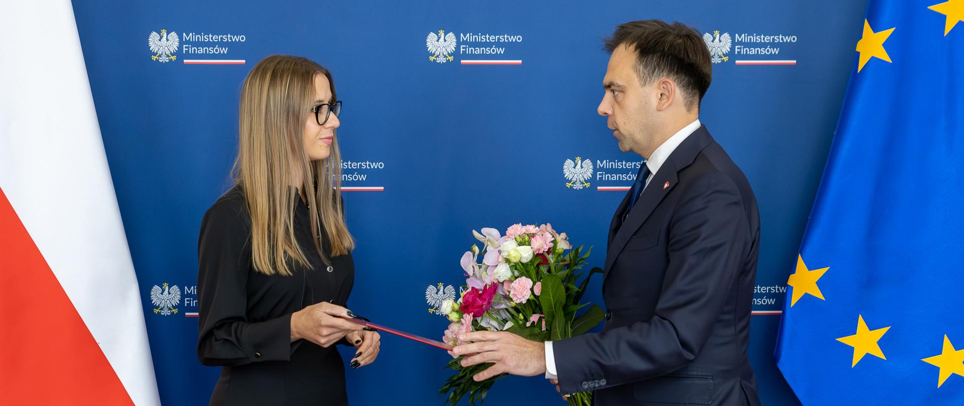 Minister Finansów i Gospodarki Andrzej Domański i Zastępca Szefa KAS Małgorzata Krok na tle ścianki oraz flag PL i UE