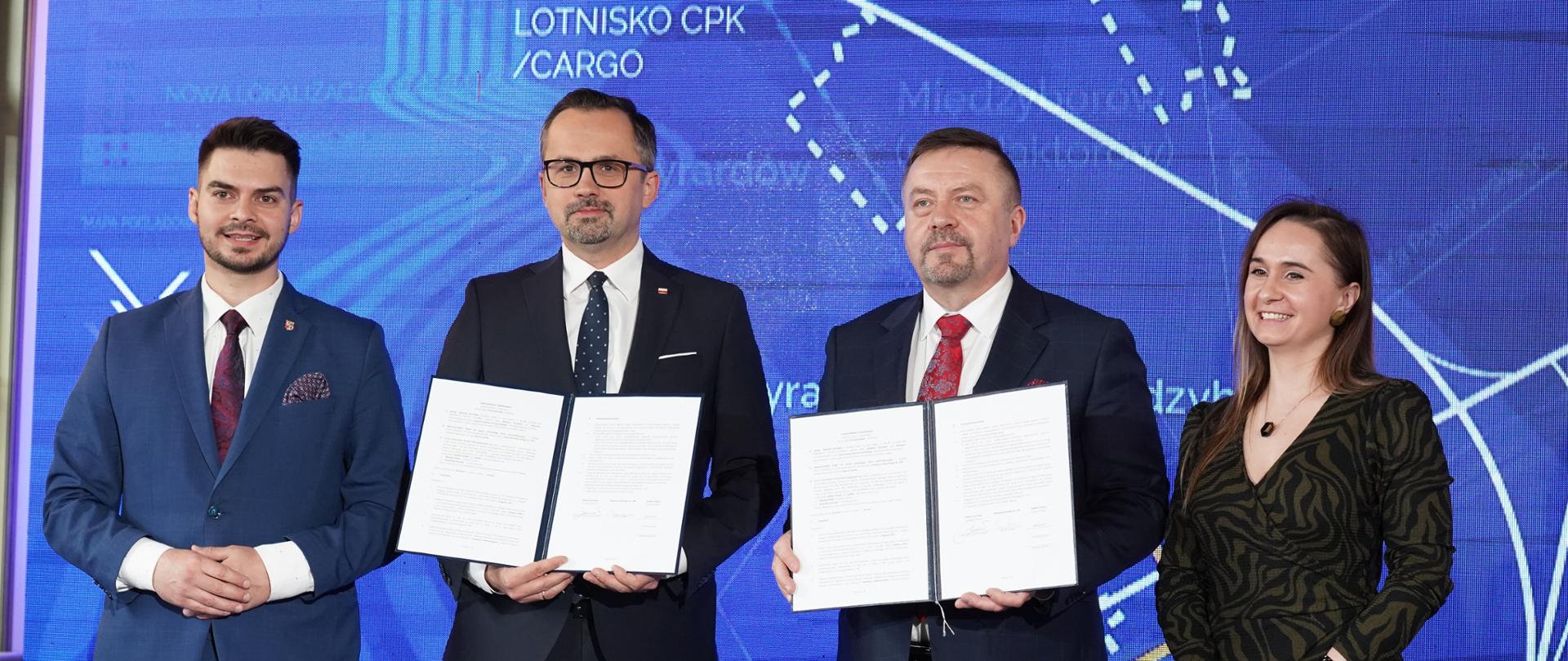 Cztery osoby stoją obok siebie. Dwie z nich trzymają akt porozumienia.