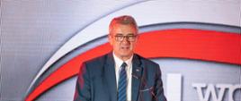 Wiceminister Murdzek stoi za mównicą i mówi do mikrofonu, przed nim dużo ludzi.