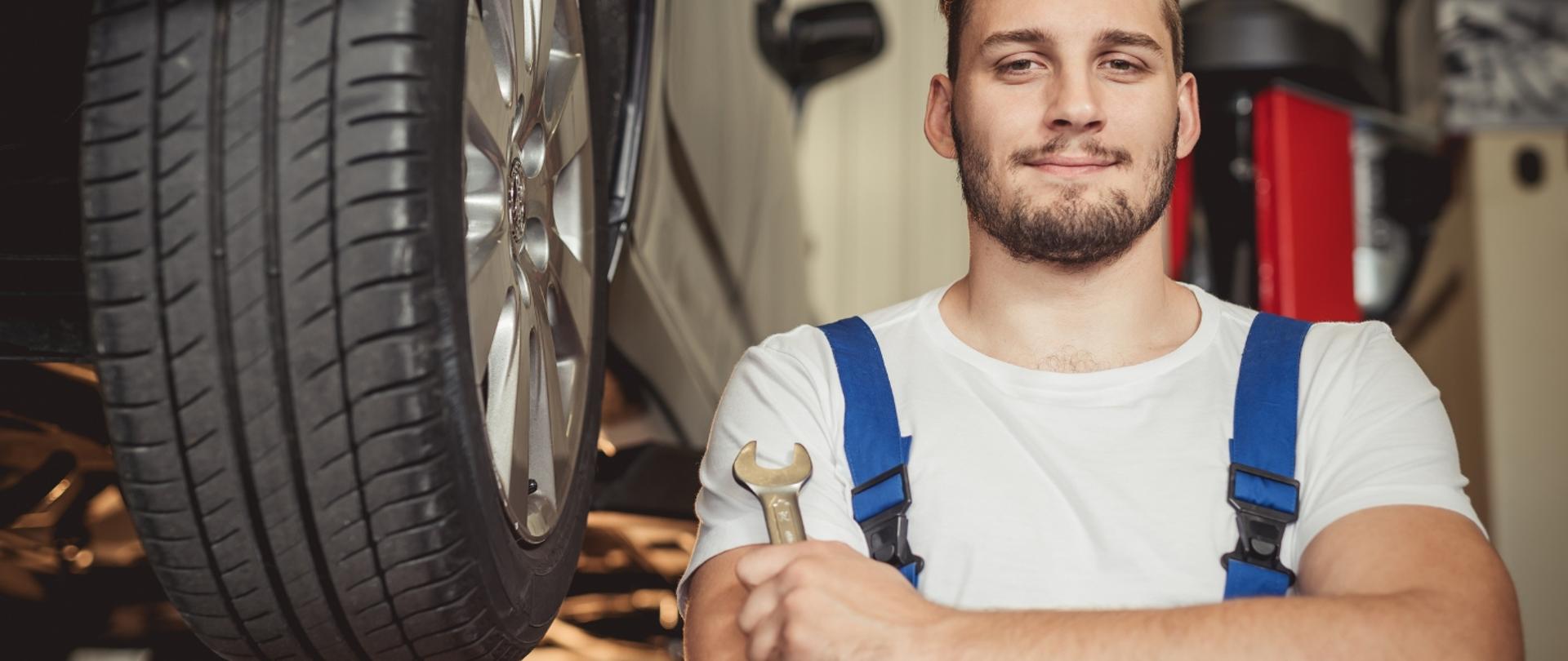 na grafice widoczny jest mechanik pojazdów elektrycznych i hybrydowych, który trzyma w dłoni klucz