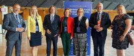 Grupa osób stoi na środku dużej sali, za nimi plakat z napisem EuroScience Open Forum.