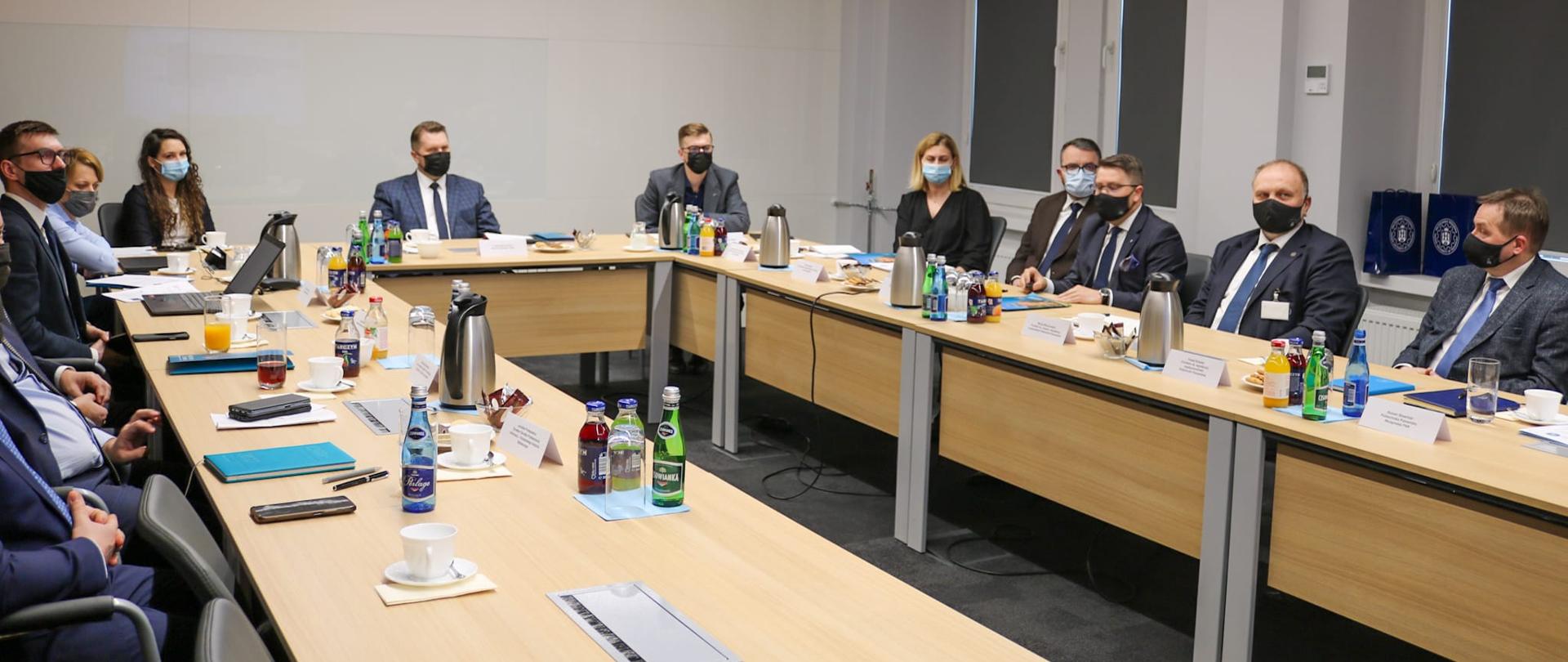 Podczas spotkania minister praz inni członkowie siedzą przy stole ustawionym w prostokąt. 