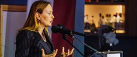 Minister Katarzyna Pełczyńska-Nałęcz stoi z lewej strony przy pulpicie i mówi do mikrofonu. 