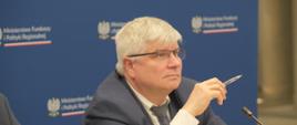 Minister Maciej Lasek siedzi przed mikrofonem.