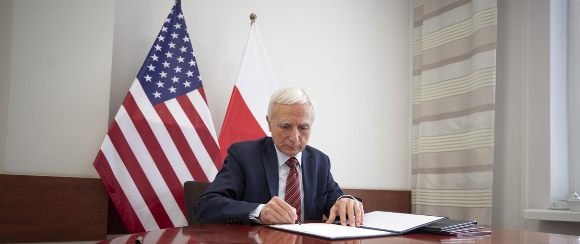 Minister Piotr Naimski siedzi przy stole.