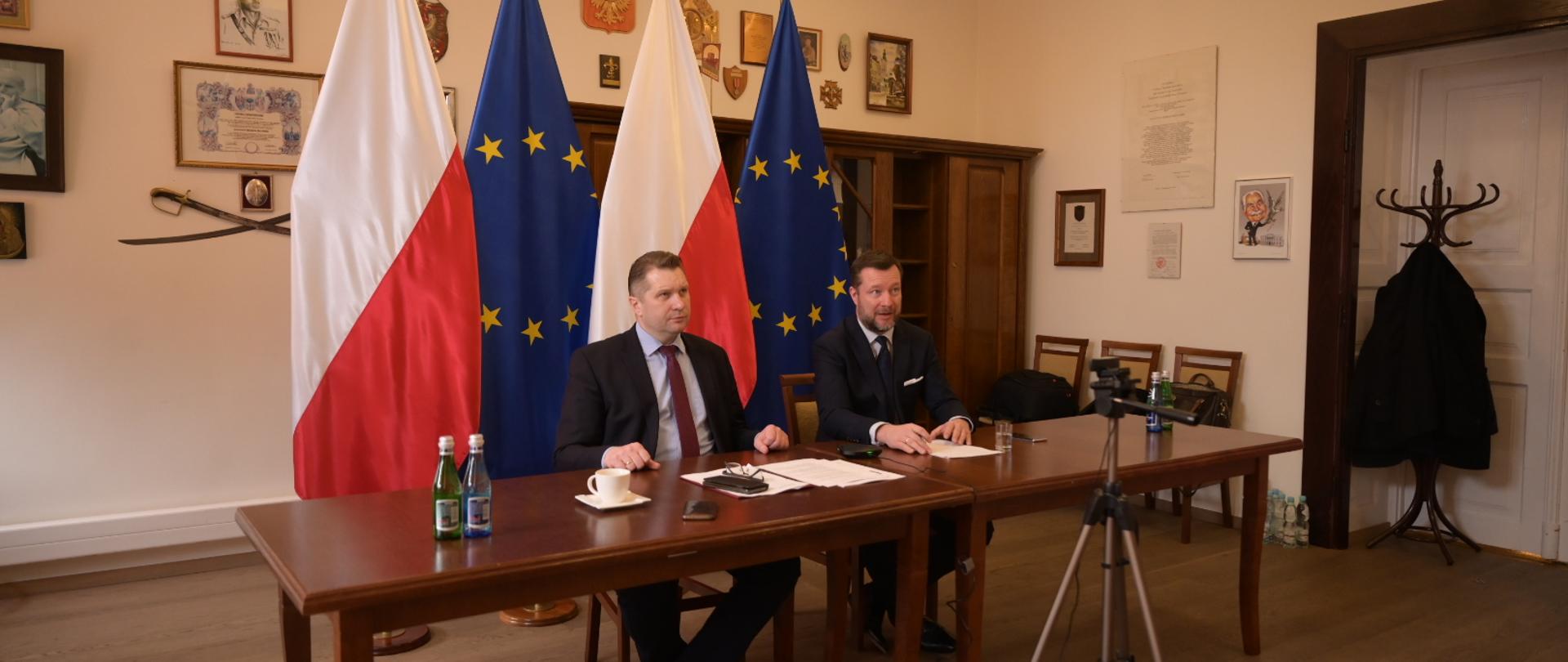 Rozmowa szefa MEiN z komisarz UE ds. innowacji, badań, kultury, edukacji i młodzieży Mariyą Gabriel. W pokoju siedzą przy stole dwie osoby ubrane w garnitur. w tle flagi Polski i Unii Europejskiej