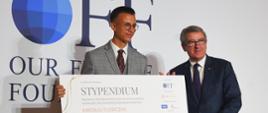 Minister Murdzek stoi obok mężczyzny w jasnym garniturze trzymającego kartkę z napisem STYPENDIUM, za nimi ścianka z napisem OFF.