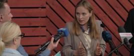Minister funduszy funduszy i polityki regionalnej Katarzyna Pełczyńska-Nałęcz stoi przy mikrofonach, obok niej dwójka dziennikarzy