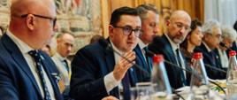 Minister Energii Miłosz Motyka przemawia przy długim stole podczas Konferencji Ministerialnej IEA w Paryżu. Wokół siedzą inni uczestnicy konfrencji