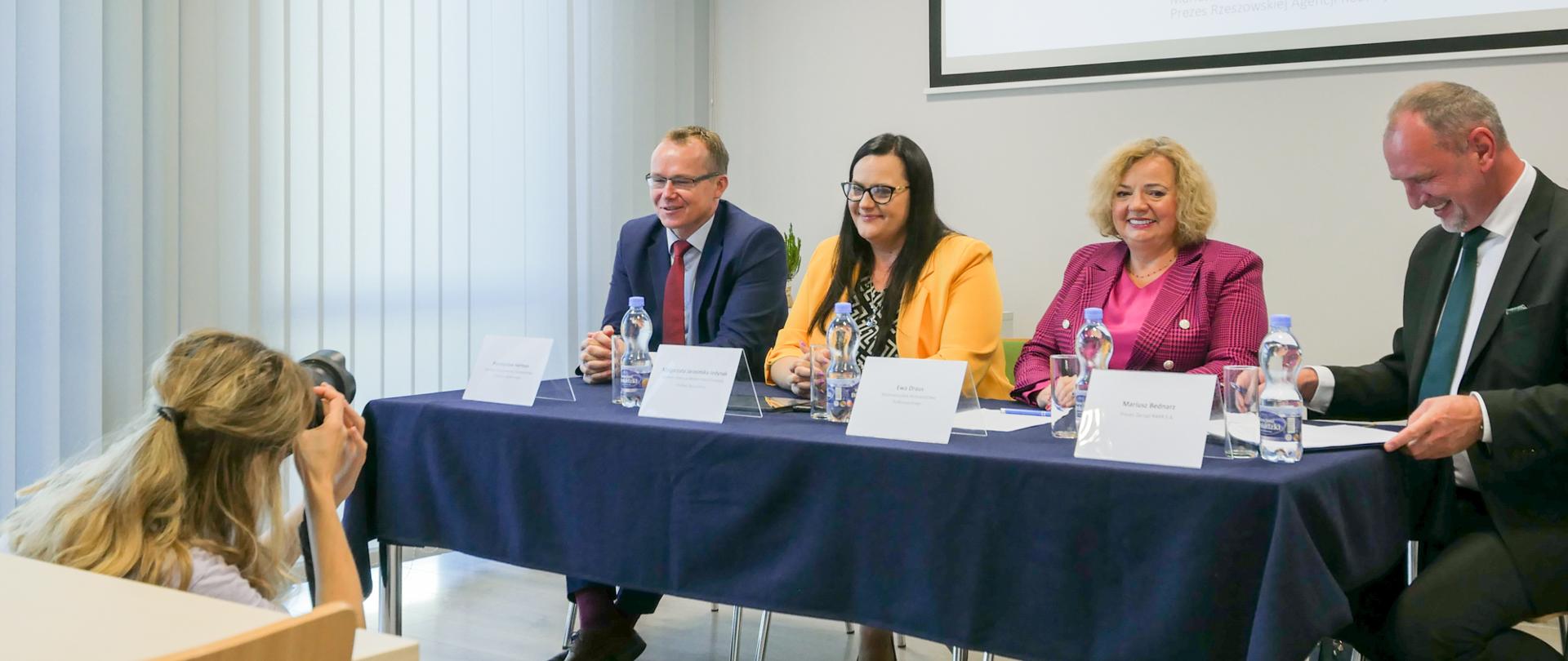 Cztery osoby siedzą przy stole. Druga od lewej wiceminister Małgorzata Jarosińska-Jedynak. Przed nimi fotograf.