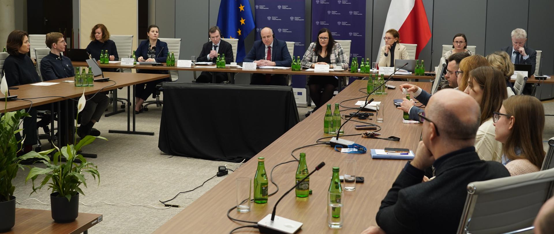 Grupa osób na sali konferencyjnej siedzi przy stołach