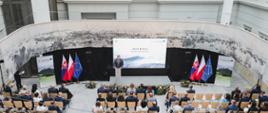 Minister Grzegorz Puda stoi przy mównicy, przemawia do uczestników konferencji siedzących na krzesłach
