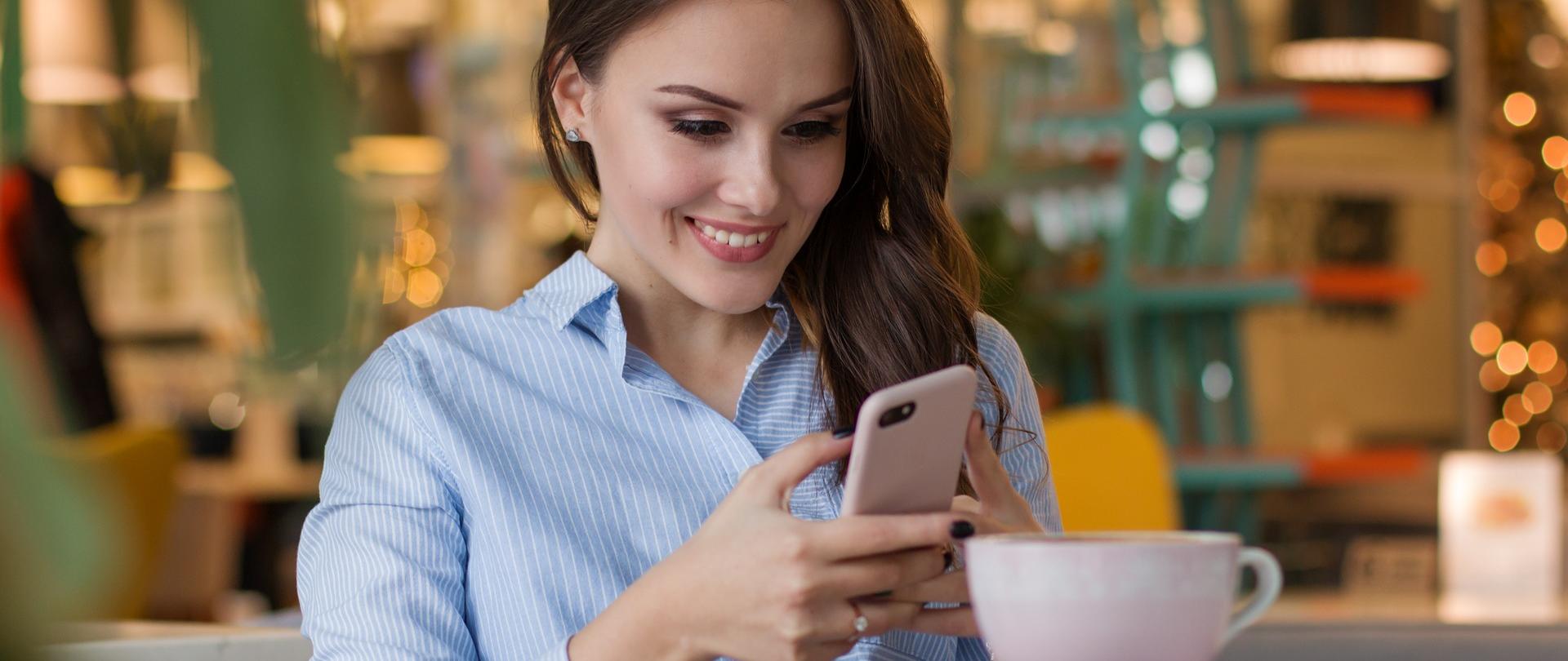 Kobieta siedząca przy filiżance kawy i pracująca na smartfonie.