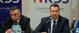 Za stołem siedzi minister Czarnek i mężczyzna w garniturze, minister mówi do stojącego przed nim mikrofonu, za nimi banery z napisem WRDS.