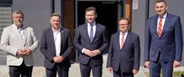 Minister Kamil Bortniczuk stoi przed wejściem do budynku wraz z gośćmi biorącymi udział w uroczystości otwarcia internatu sportowego w Centralnym Ośrodku Sportu Cetniewo