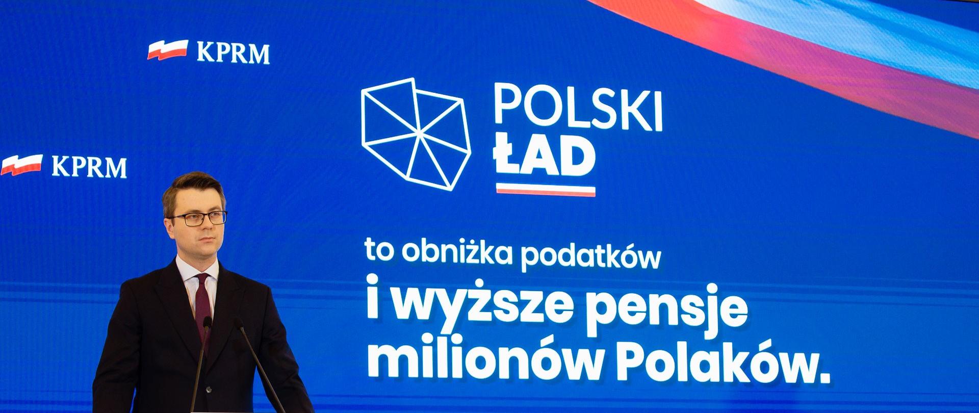 Rzecznik rządu przy mównicy podczas konferencji.