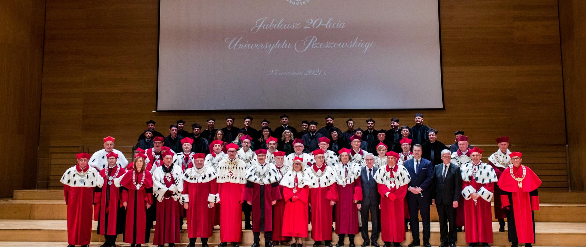 Jubileusz-20-lecia Uniwersytetu Rzeszowskiego z udziałem Ministra Edukacji i Nauki Przemysława Czarnka, na zdjęciu włacze uczelni w czerwonych i czarnych togach w tle napis jubileusz 20-lecia UR