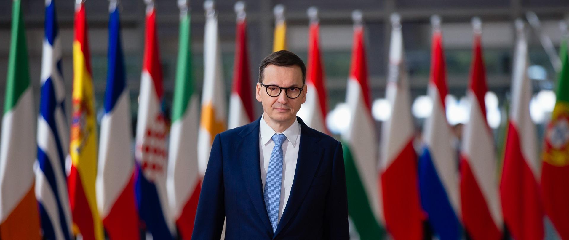 Premier Mateusz Morawiecki w trakcie przerwy posiedzenia Rady Europejskiej w Brukseli, w tle flagi państw UE.