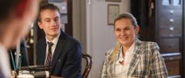 Minister Edukacji siedzi przy stole i rozmawia z przedstawicielami samorządu uczniowskiego. Obok niej siedzi uczeń.