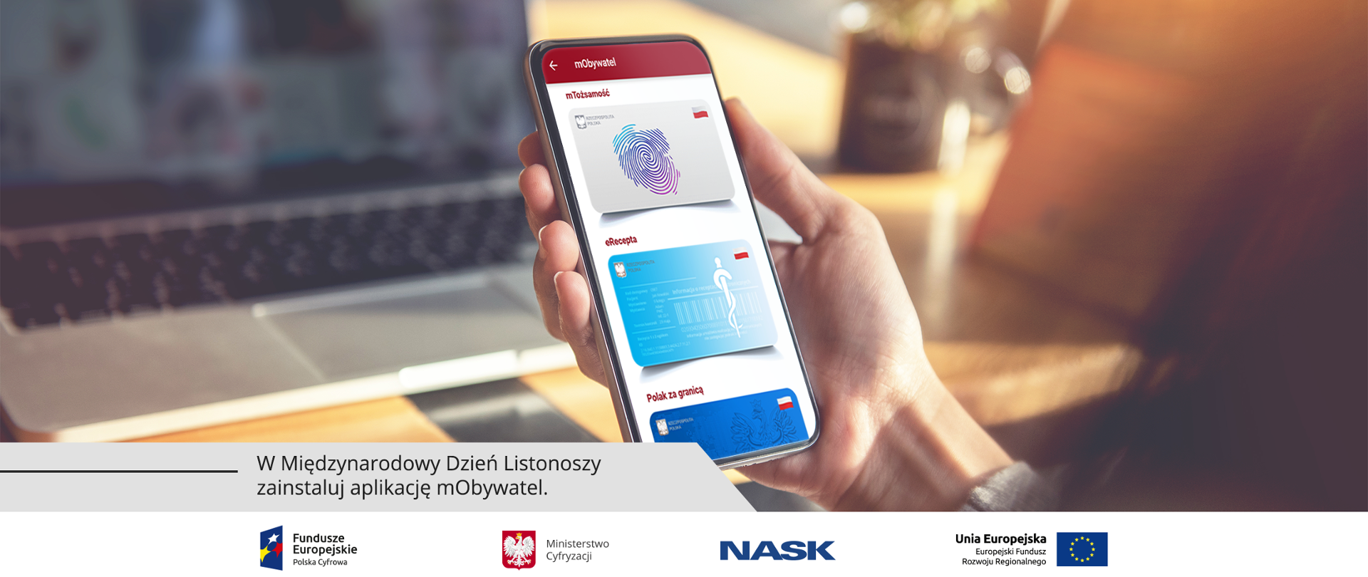 Na pierwszym planie telefon w kobiecej dłoni z aplikacją mObywatel wyświetlaną na ekranie. W tle stolik kawiarniany z laptopem na blacie. Napis: W Międzynarodowy Dzień Listonoszy zainstaluj aplikację mObywatel.