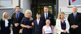 Przed wejściem do budynku stoi minister Czarnek otoczony przez kilka osób.