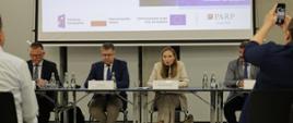 Minister funduszy i polityki regionalnej Katarzyna Pełczyńska-Nałęcz na spotkaniu z przedsiębiorcami woj. opolskiego, minister siedzi przy stole i przemawia do mikrofonu