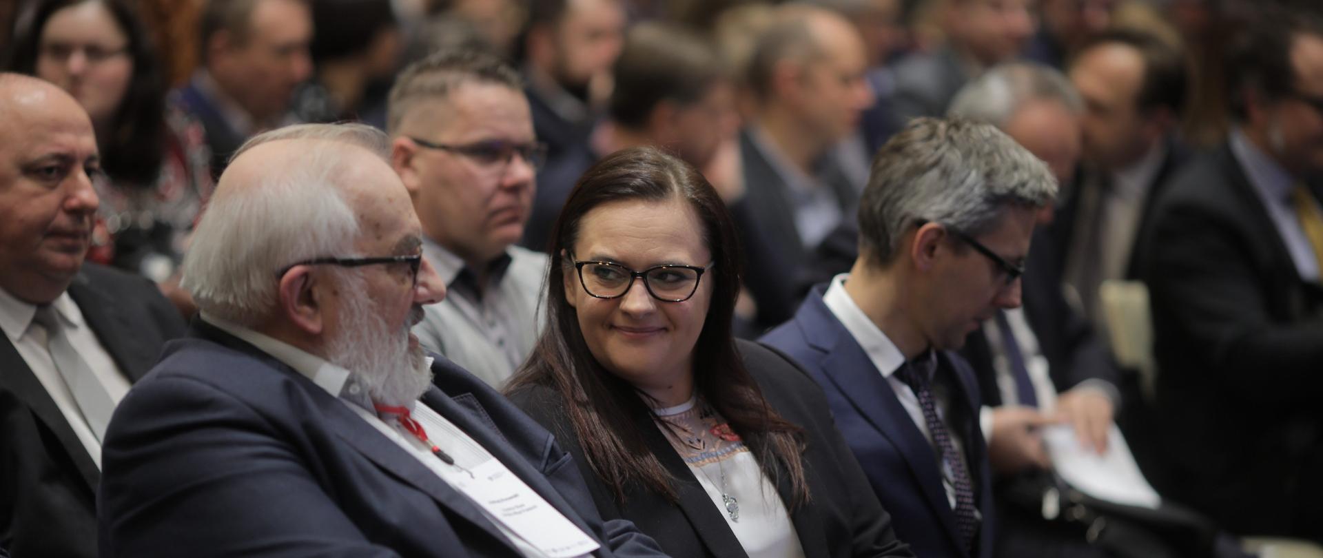 wśród wielu siedzących na sali podczas konferencji osób na środku zdjęcia widoczna minister Małgorzata Jarosińska-Jedynak podczas rozmowy z Andrzejem Porawskim, dyrektorem biura Związku Miast Polskich