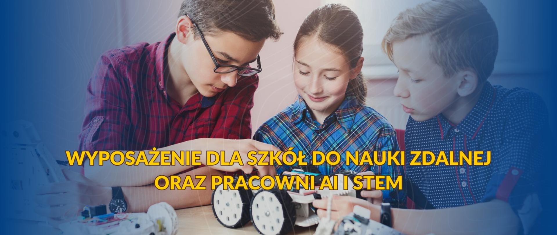 Troje młodych ludzi pochyla się nad stołem, pracując wspólnie nad projektem robotycznym. Chłopak po lewej, w okularach i bordowo-granatowej koszuli w kratę, uważnie przygląda się elementom robota. Dziewczyna w środku, w niebiesko-białej koszuli w kratę, z uśmiechem manipuluje przy białych kołach robota. Chłopak po prawej, w niebieskiej koszuli w drobne wzory, również skupia się na robocie.
Na stole rozłożone są różne części robota, w tym białe i czarne elementy konstrukcyjne, koła oraz przewody. W tle widoczna jest rozmyta przestrzeń, sugerująca wnętrze. Na pierwszym planie, nałożony na obraz, znajduje się półprzezroczysty żółty tekst w języku polskim: "WYPOSAŻENIE DLA SZKÓŁ DO NAUKI ZDALNEJ ORAZ PRACOWNI AI I STEM".