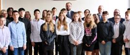 Grupa młodych ludzi stoi pod koszem do koszykówki, pośród nich kilku dorosłych mężczyzn i kobiet.
