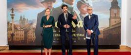 Barbara Nowacka, Maciej Kawalski oraz Andrzej Seweryn stoją na czerwonym dywanie przy mikrofonach. W tle znajduje się wielki plakat filmu „Lalka” z napisem „Epicka ekranizacja powieści Bolesława Prusa”.