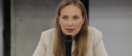 Minister funduszy i polityki regionalnej Katarzyna Pełczyńska-Nałęcz na spotkaniu z przedsiębiorcami woj. opolskiego, minister siedzi przy stole i przemawia do mikrofonu