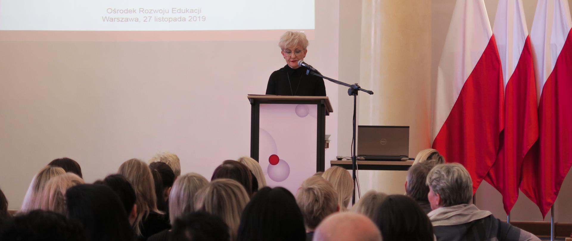 Iwona Michałek – wiceminister Edukacji Narodowej – przemawia na gali, w tle polskie flagi