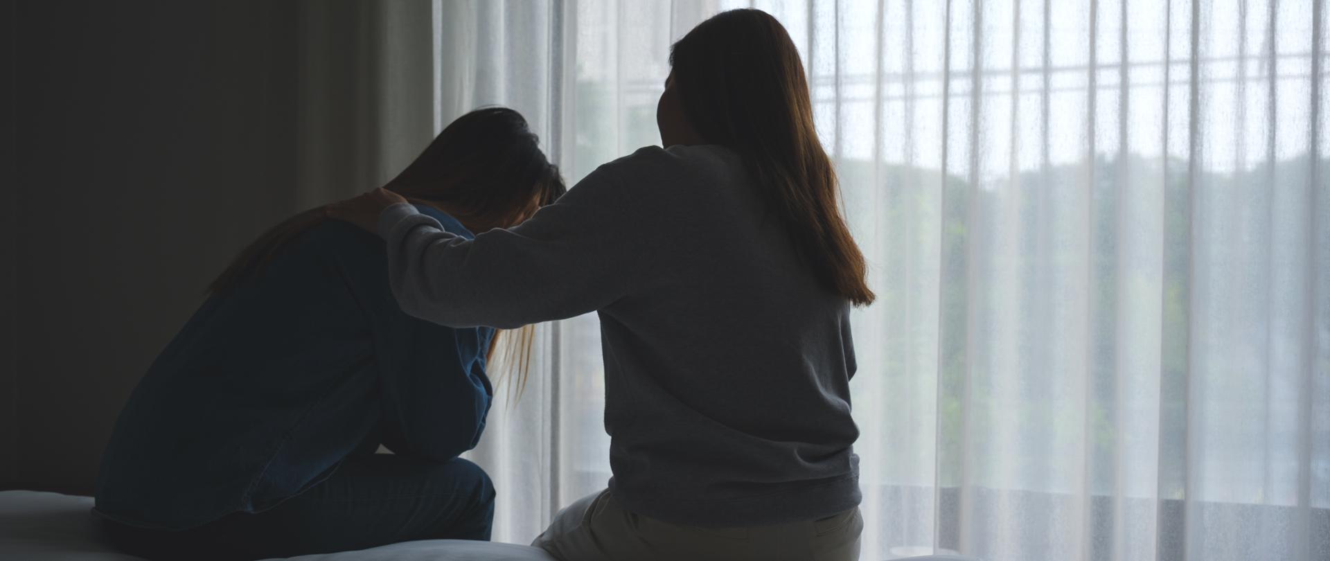 Silhouette image of a woman touching her friend shoulder to comforting and giving encouragement in bedroom