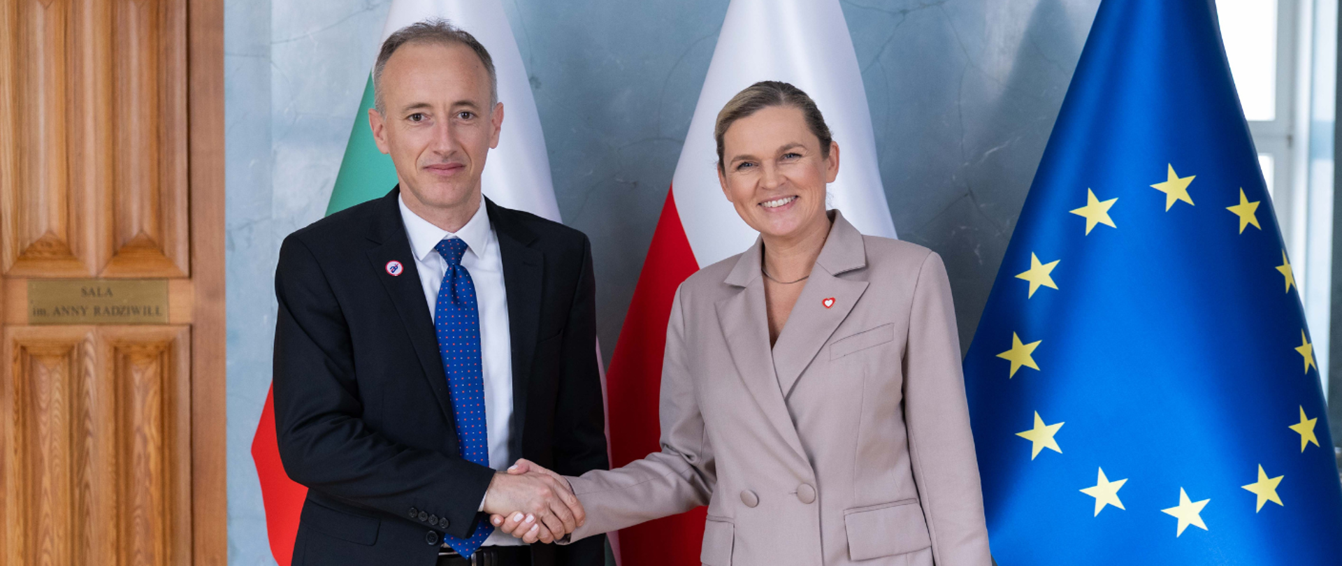 spotkanie z Ministrem Edukacji i Nauki Bułgarii, minister Edukacji Polski wraz z ministrem edukacji Bułgarii podają sobie ręce na tle flag.