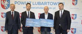 Pod ścianką z napisem Powiat Lubartowski stoi minister Czarnek i trzech mężczyzn w garniturach, dwóch trzyma tabliczki z napisami Gmina Kock.
