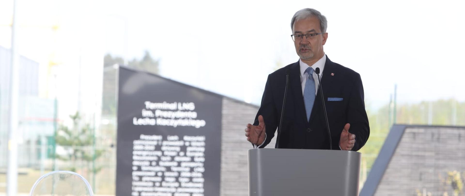 Minister Jerzy Kwieciński stoi przy mównicy. 
