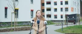 Na zdjęciu minister Katarzyna Pełczyńska-Nałęcz stoi przed mikrofonami i odpowiada na pytania dziennikarzy