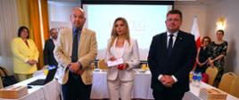 Mężczyzna w żółtej marynarce, kobieta w białym ubraniu i minister Rzymkowski stoją obok siebie i patrzą w obiektyw.