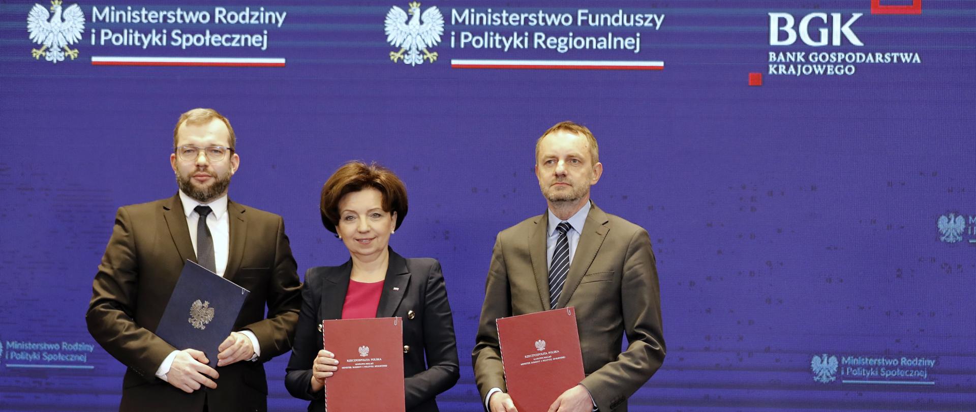  Trzy osoby stoją obok siebie i trzymają w dłoniach teczki z logo orła.