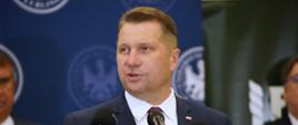 Minister Czarnek mówi do kilku mikrofonów na stojakach.