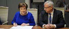 Podpisanie umów na dofinansowanie rozwoju dróg wojewódzkich w Polsce Wschodniej, kobieta siedzi przy stole i podpisuje dokument, obok niej po prawej przedstawiciel województwa mazowieckiego