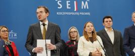 Minister funduszy i polityki regionalnej Katarzyna Pełczyńska-Nałęcz stoi przed mikrofonem, po jej prawej stronie stoi przed mikrofonem wiceminister Jan Szyszko, który trzyma w dłoniach kartkę, za nimi stoją posłowie 
